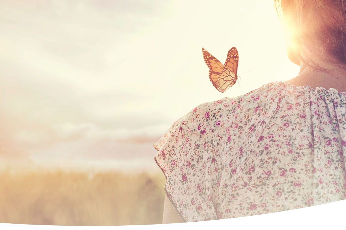 butterfly on a womans shoulder with the sunset glistening in the background